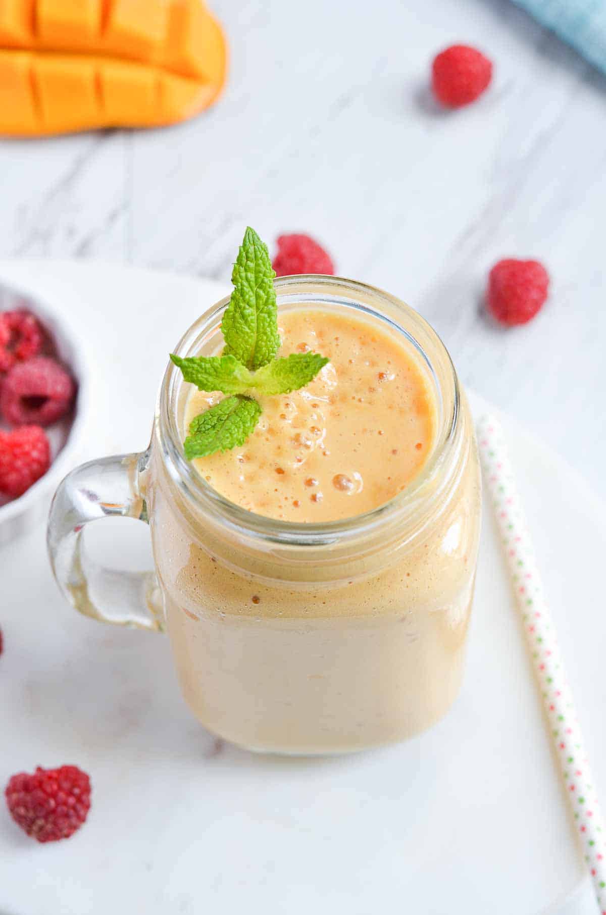 mango raspberry smoothie served in a glass jar with mint leaves.
