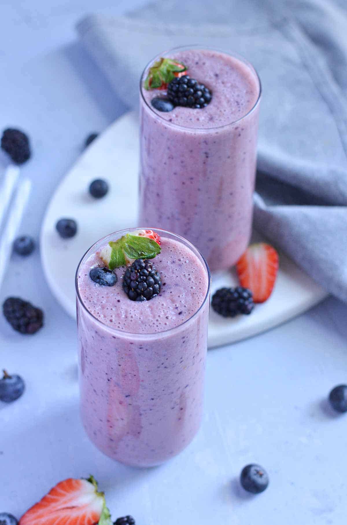 triple berry smoothie served in two glasses, garnished with blackberry.