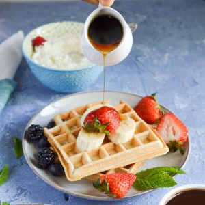 close up click of wheat waffles served with berries, banana and maple syrup.