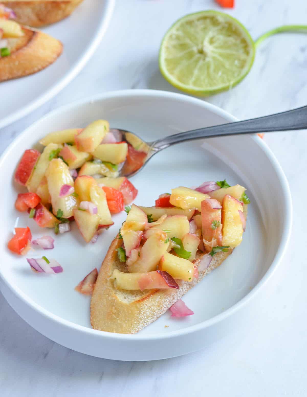 Peach salsa crostini served in a single plate with the spoon.
