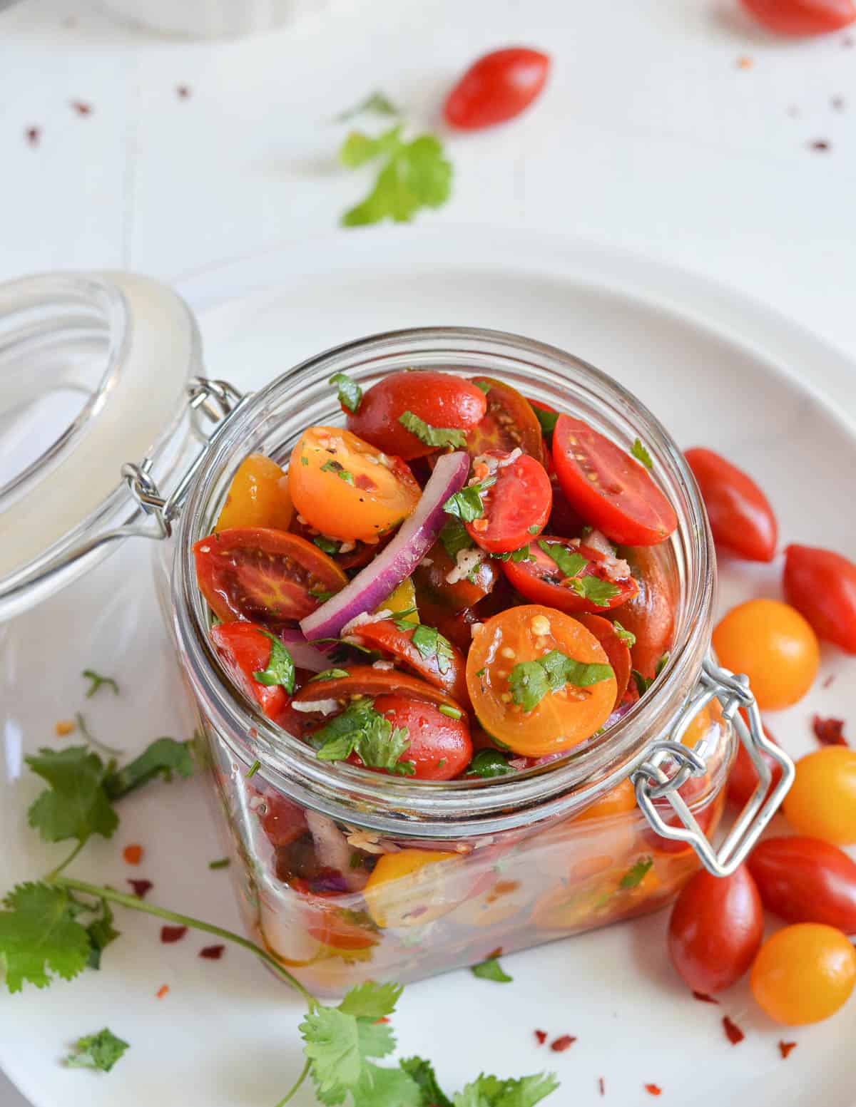 prepared tomato salad in the glass jar surrounded with extra cherry tomatoes.