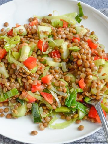 warm brown lentil salad served in white plate along with a fork.