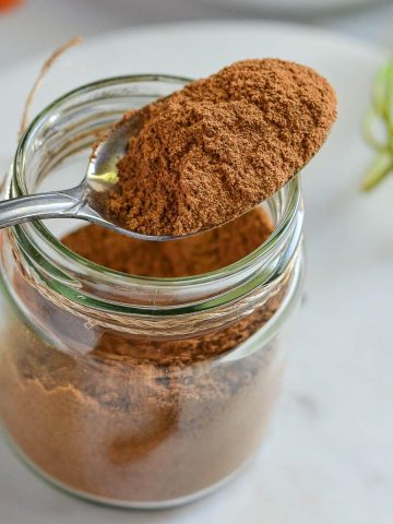 pumpkin pie spice blend is in glass jar, spoonful spice blend is shown closely.