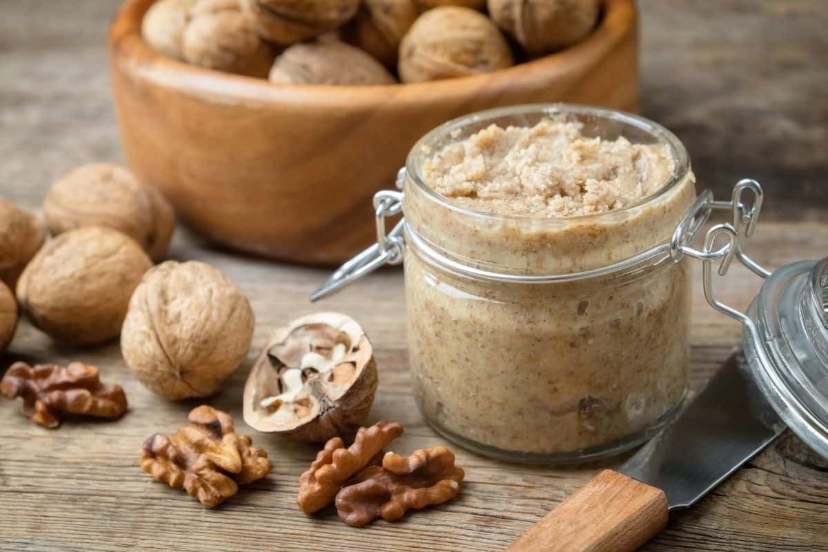 walnut butter in a jar and surrounded by broken walnuts.
