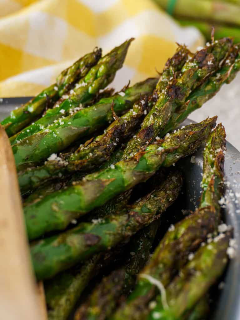 Close-up of grilled asparagus with visible grill marks and melted parmesan, against a soft yellow napkin.