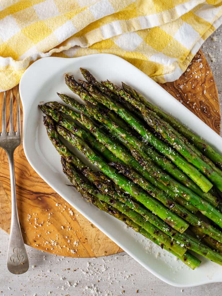 Overhead image of grilled asparagus on a platter, salt flakes scattered across the plate and napkin nearby.