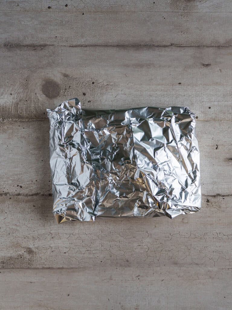 Foil packet sealed tightly around parchment-wrapped asparagus, ready for grilling.